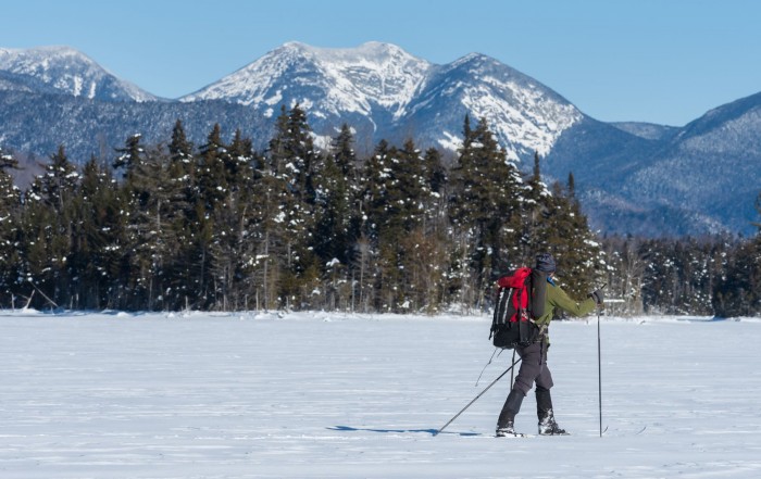 A man skis on a frozen lake while looking at a mountain
