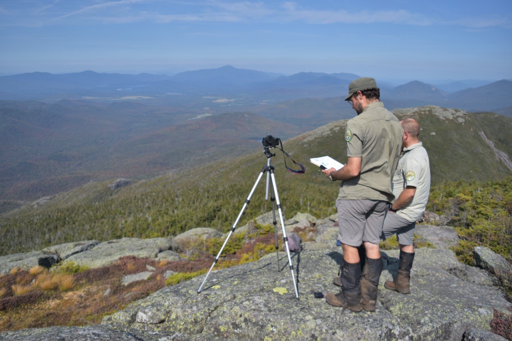 Two people stand behind a camera on a mountain